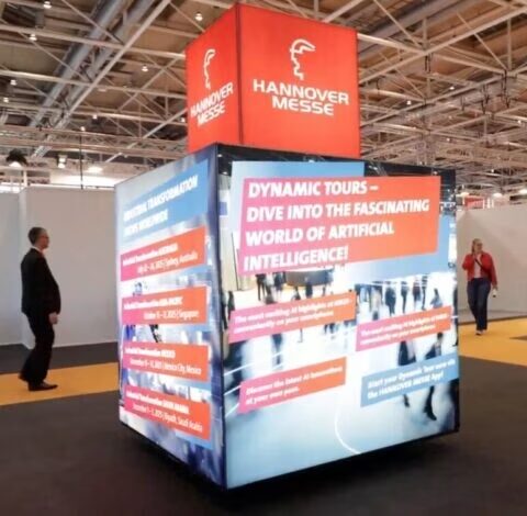 Beleuchteter Dynamic-Tours-Würfel der Hannover Messe in der Messehalle mit vorbeigehenden Besuchern